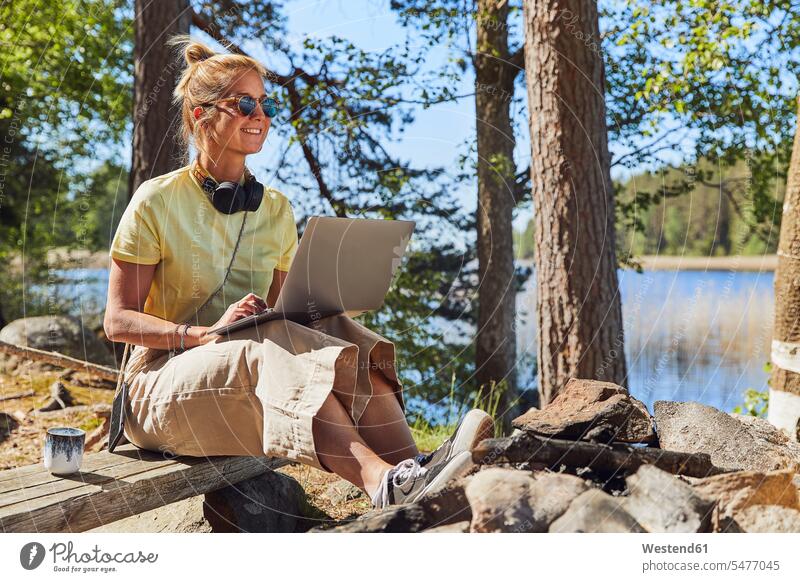Mittelgroße erwachsene Frau mit Sonnenbrille und Laptop im Tiveden-Nationalpark, Schweden Farbaufnahme Farbe Farbfoto Farbphoto Skandinavien