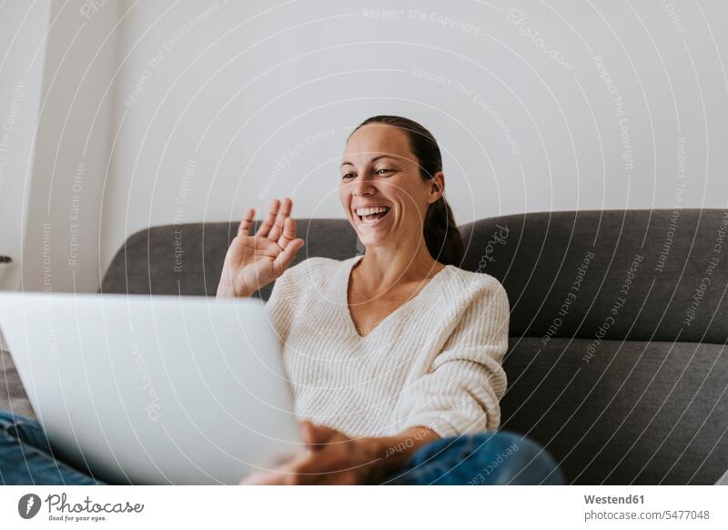 Glückliche Frau winkt mit der Hand Videoanruf am Laptop zu Hause Farbaufnahme Farbe Farbfoto Farbphoto Verbindung verbunden Anschluss verbinden Zuhause