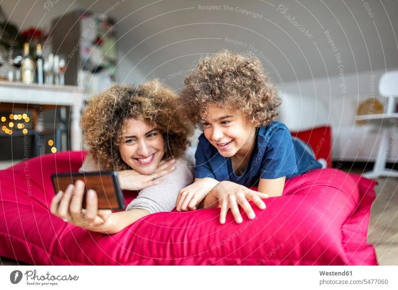 Mutter und Sohn sehen sich ein Video auf einem Smartphone an und liegen auf einem großen Kissen Polster Telekommunikation telefonieren Handies Handys