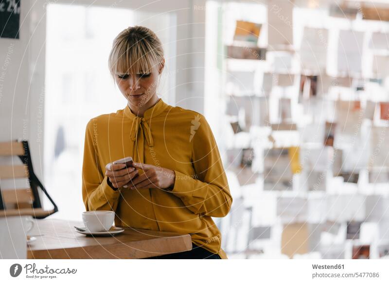 Blonde Geschäftsfrau mit Smartphone in einem Café, Lesen von Textnachrichten SMS iPhone Smartphones Portrait Porträts Portraits sitzen sitzend sitzt benutzen