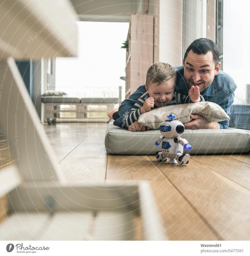 Aufgeregter Vater und Sohn liegen auf einer Matratze zu Hause und beobachten einen Spielzeugroboter liegend liegt Zuhause daheim Aufregung aufregend