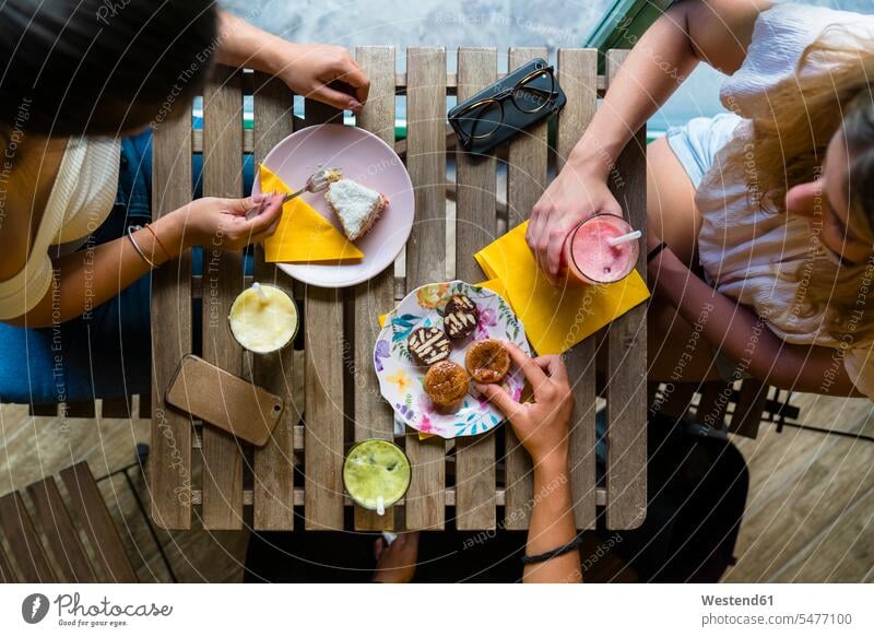 Draufsicht auf drei junge Frauen, die an einem Holztisch mit Smoothies und Keksen sitzen Leute Menschen People Person Personen Europäisch Kaukasier kaukasisch
