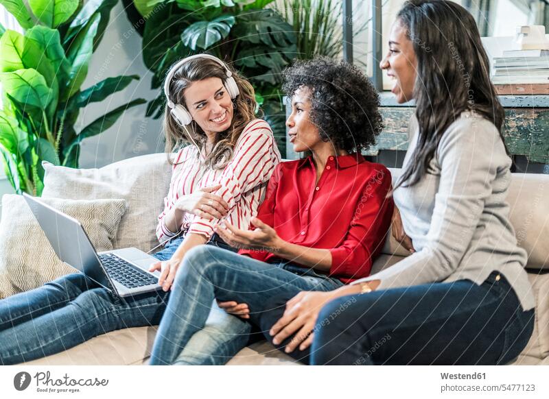 Drei glückliche Frauen mit Laptop sitzen auf Couch sitzend sitzt weiblich Freundinnen Sofa Couches Liege Sofas Notebook Laptops Notebooks Glück glücklich sein