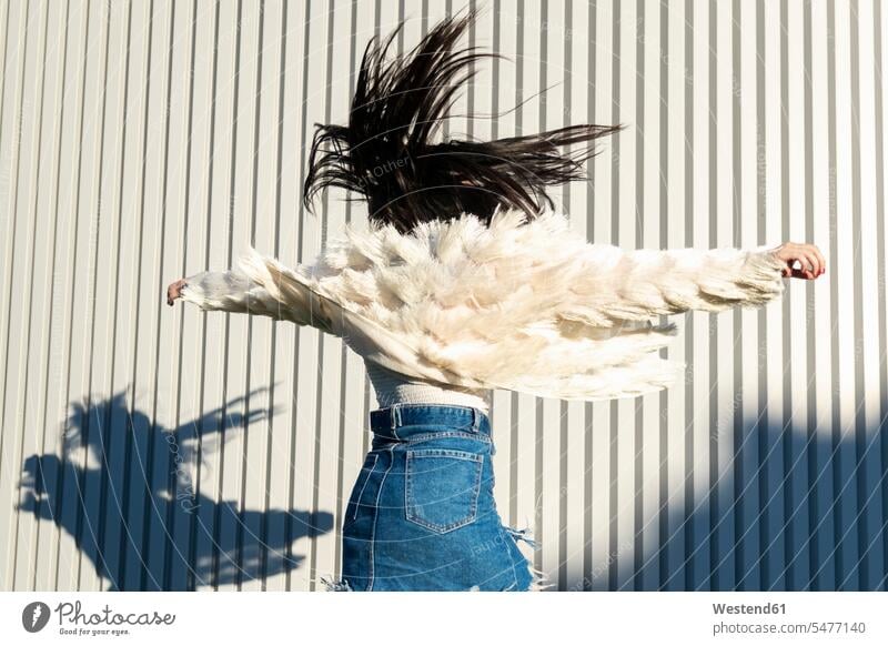 Unbekümmerte junge Frau mit ausgestreckten Armen tanzt gegen die weiße Mauer in der Stadt Farbaufnahme Farbe Farbfoto Farbphoto Freizeitbeschäftigung Muße Zeit