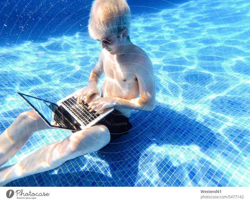 Junger Mann ohne Hemd und mit Sonnenbrille mit Laptop unter Wasser im Schwimmbad Farbaufnahme Farbe Farbfoto Farbphoto Spanien Freizeitbeschäftigung Muße Zeit