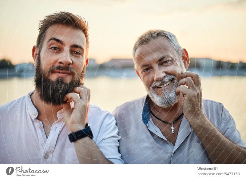 Porträt eines lächelnden Vaters und eines erwachsenen Sohnes, die sich an ihren Bärten kratzen Generation Hemden abends sommerlich Sommerzeit entspannen relaxen
