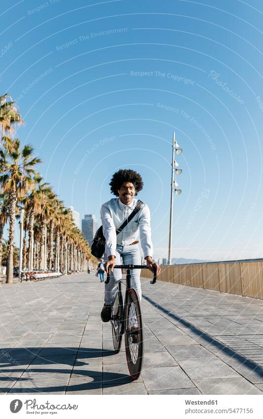 Mittlerer erwachsener Mann fährt Fahrrad auf einer Strandpromenade, hört Musik Bikes Fahrräder Räder Rad Ohrhörer fahren Strandpromenaden Musik hören radfahren