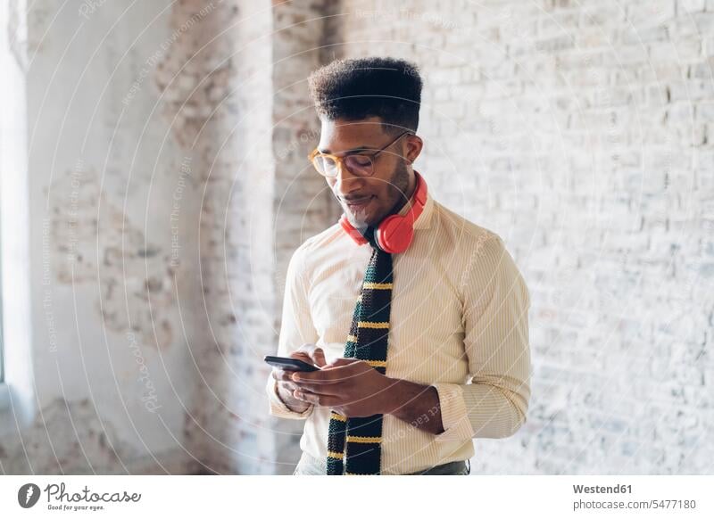 Stilvoller junger Mann benutzt Smartphone im Loft Leute Menschen People Person Personen gemischtrassig 1 Ein ein Mensch eine nur eine Person single erwachsen