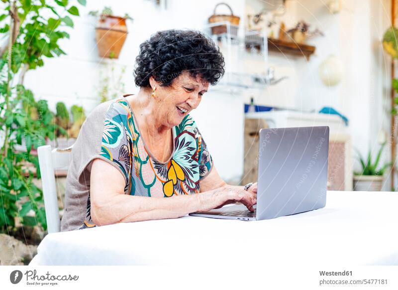 Glückliche ältere Frau benutzt Laptop auf dem Tisch, während sie im Hof sitzt Farbaufnahme Farbe Farbfoto Farbphoto Spanien Freizeitbeschäftigung Muße Zeit