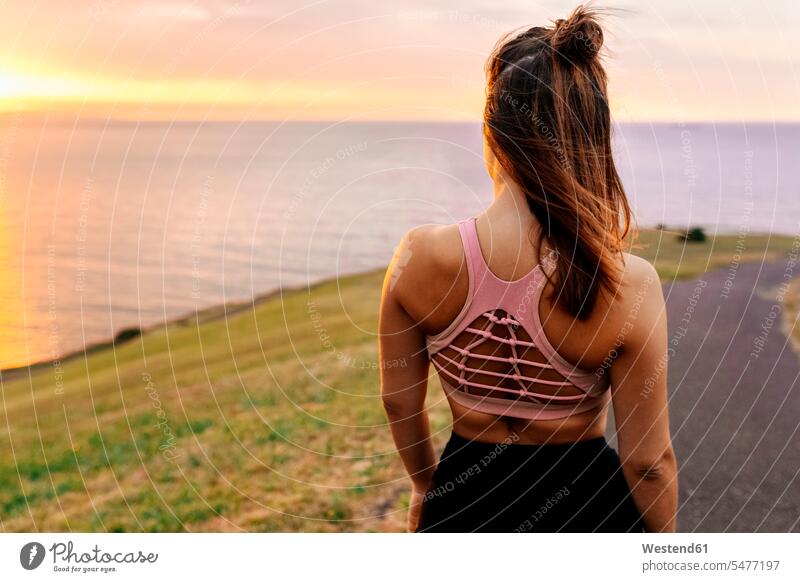Junge Sportlerin schaut bei Sonnenuntergang aufs Meer Farbaufnahme Farbe Farbfoto Farbphoto Außenaufnahme außen draußen im Freien Rückansicht Rückenansicht