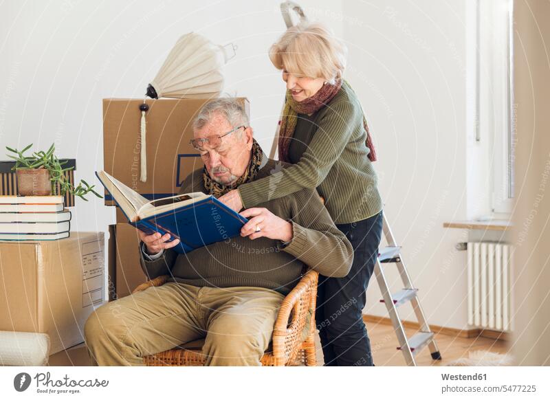 Älteres Ehepaar betrachtet Fotoalbum umgeben von Pappkartons in einem leeren Raum Leute Menschen People Person Personen Europäisch Kaukasier kaukasisch 2