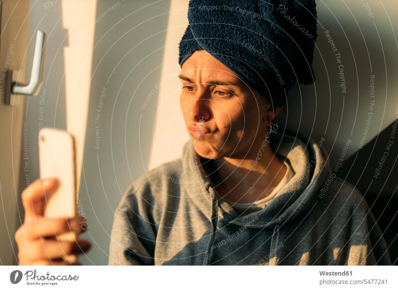 Junge Frau, die zu Hause auf ihr Handy schmollt Telekommunikation telefonieren Handies Handys Mobiltelefon Mobiltelefone Lektüre Gesichtsausdruck Mienenspiel