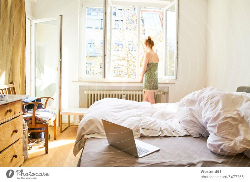 Rückenansicht einer Frau im Schlafzimmer, die aus dem Fenster schaut schauen schauend anschauen betrachten weiblich Frauen stehen stehend steht sehend Zimmer