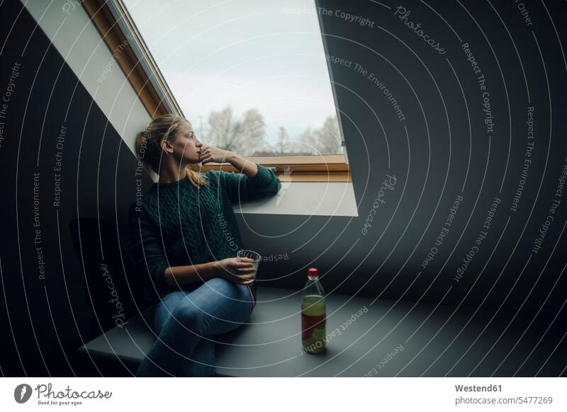 Junge Frau schaut aus dem Dachbodenfenster Deutschland ausruhen Rast Erholung erholen Wohnung wohnen Wohnungen denken nachdenken Dachfenster überlegen Mansarde