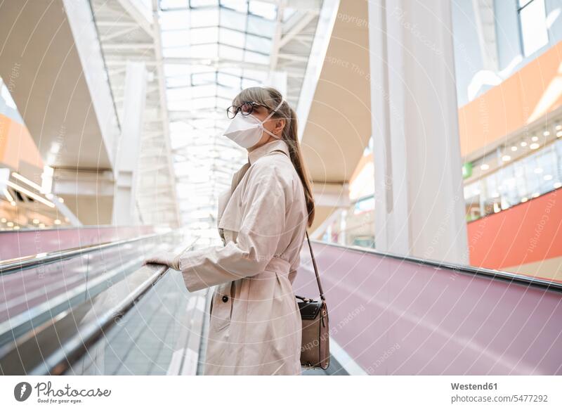 Frau mit Gesichtsmaske und Einweghandschuhen auf einer Rolltreppe in einem Einkaufszentrum Taschen Handtaschen Brillen Fahrtreppe Kauf Einkaufen shoppen