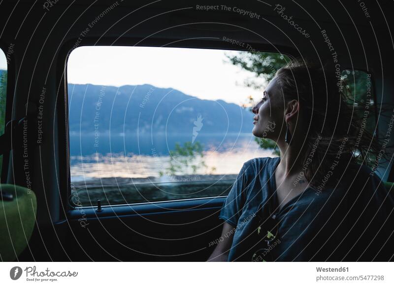 Junge Frau sitzt auf der Rückbank in einem Auto und schaut aus dem Fenster weiblich Frauen schauen schauend anschauen betrachten Rücksitz Ruecksitz Ruecksitze