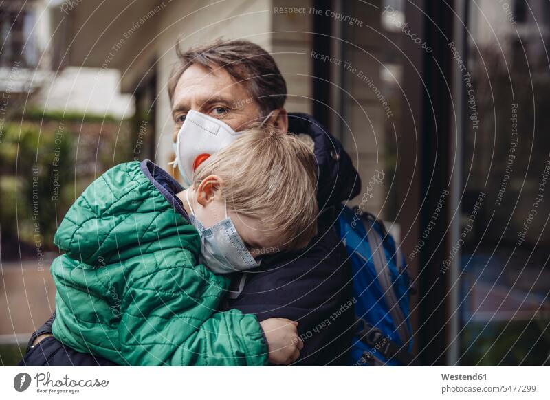 Vater trägt Sohn, beide tragen Schutzmasken, im Freien Rucksäcke Gesundheit Gesundheitswesen medizinisch Erkrankung Erkrankungen Krankheiten geschützt schützen