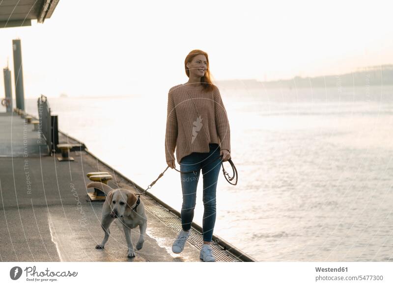 Deutschland, Hamburg, Frau spaziert mit Hund auf Pier am Elbufer weiblich Frauen Landungssteg Piers Flussufer glücklich Glück glücklich sein glücklichsein