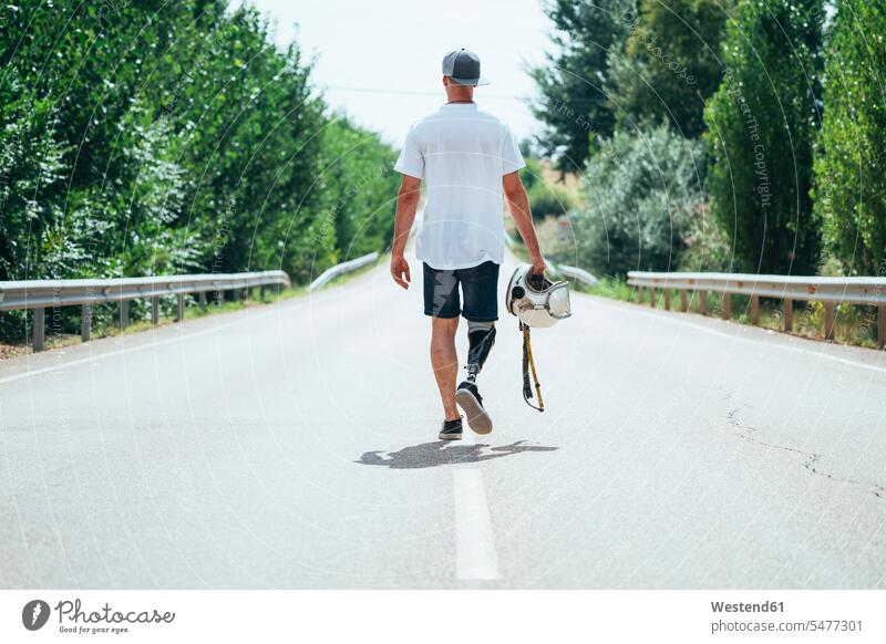 Junger Mann mit Beinprothese, der mit einem Helm die Straße entlang geht T-Shirts gehend Jahreszeiten sommerlich Sommerzeit Muße Individuell auf Achse
