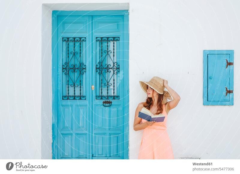 Rothaarige junge Frau mit Buch steht vor einem Haus und schaut in die Ferne, Frigiliana, Malaga, Spanien Bücher Lektüre sommerlich Sommerzeit Farben Farbtoene