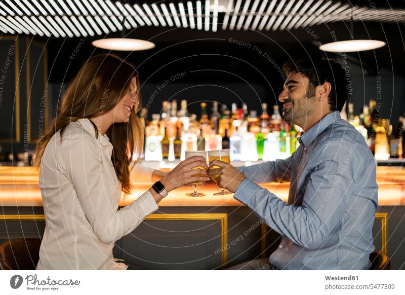 Lächelnde Paar klirren Biergläser in einer Bar Bierglas anstoßen zuprosten anstossen Bars Pärchen Paare Partnerschaft lächeln Glas Trinkgläser Gläser Trinkglas