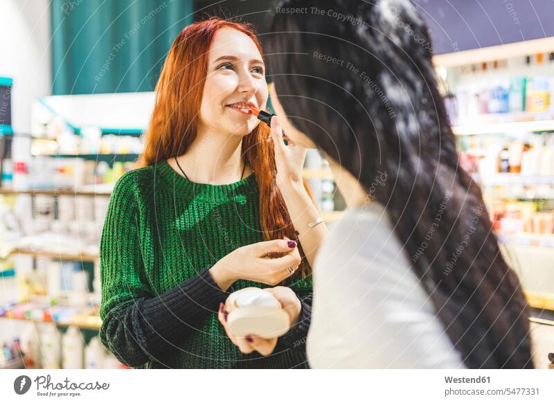 Zwei Frauen in einem Kosmetikgeschäft probieren Lippenstift aus testen Lippenstifte Geschäft Shop Laden Läden Geschäfte Shops Kundin ausprobieren Kosmetika