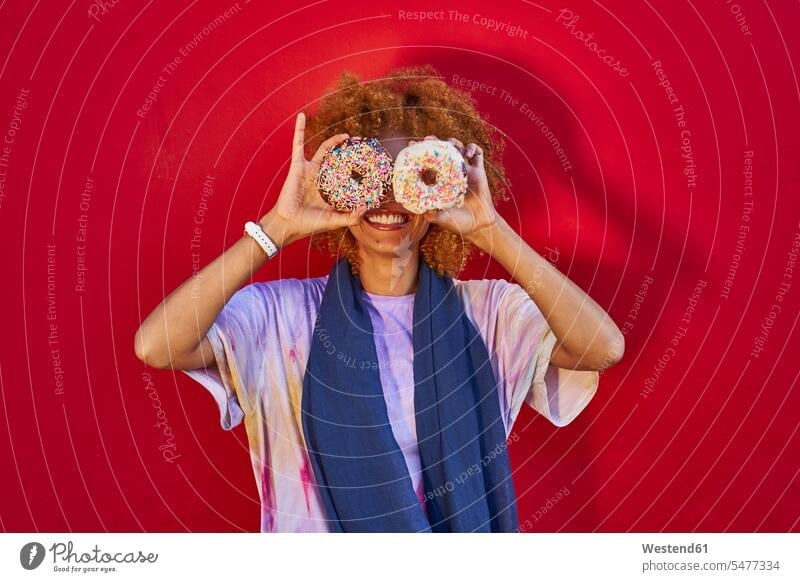 Verspielte Frau hält zwei Donuts vor ihren Augen Leute Menschen People Person Personen Afrikanisch Afrikanische Abstammung dunkelhäutig Farbige Farbiger