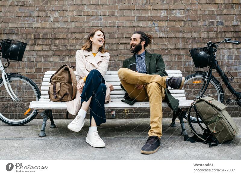 Glückliches Paar sitzt auf einer Bank neben den E-Bikes und unterhält sich eBikes Elektrofahrrad Elektrorad glücklich glücklich sein glücklichsein sprechen