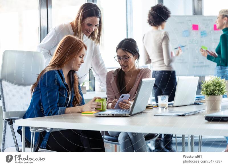 Geschäftsfrauen, die während einer Besprechung in einem Büro ein Smartphone benutzen Job Berufe Berufstätigkeit Beschäftigung Jobs geschäftlich Geschäftsleben