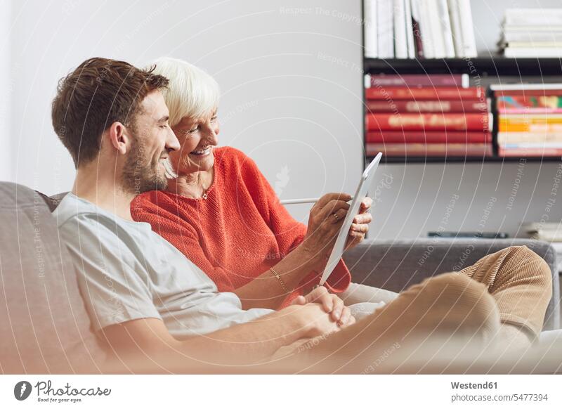 Enkel sitzt auf der Couch und benutzt ein digitales Tablet mit seiner Großmutter Leute Menschen People Person Personen erwachsen Erwachsene Frauen weiblich alt