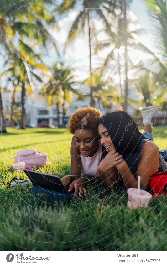 Zwei glückliche Freundinnen entspannen in einem Park mit einem Tablet entspannt entspanntheit relaxt Glück glücklich sein glücklichsein Tablet Computer