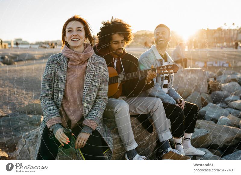 Drei glückliche Freunde mit Gitarre sitzen im Freien bei Sonnenuntergang sitzend sitzt Glück glücklich sein glücklichsein Sonnenuntergänge Gitarren Stimmung