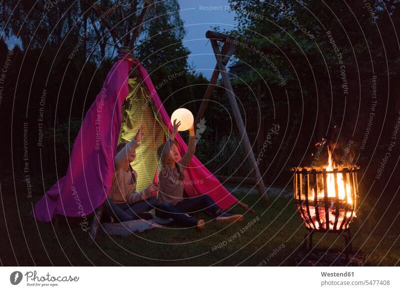 Zwei Mädchen stehen vor dem Tipi, halten Lampe als Mond Licht Lichter Lagerfeuer spielen hochhalten heben hochheben Garten Gärten Gaerten Zelt Zelte Monde