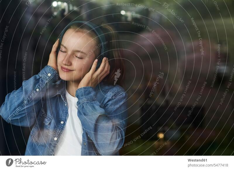Vorpubertäres Mädchen mit geschlossenen Augen, das zu Hause über Kopfhörer Musik hört Farbaufnahme Farbe Farbfoto Farbphoto Außenaufnahme außen draußen