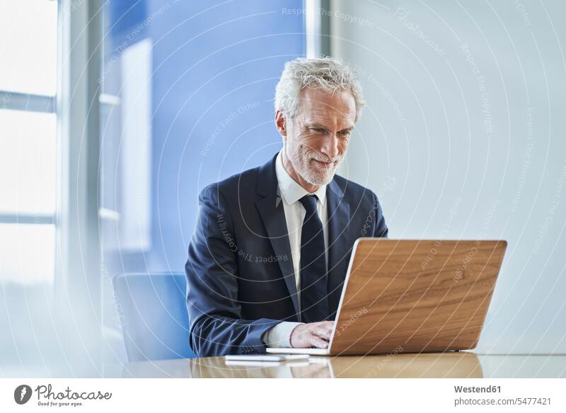 Selbstbewusster Geschäftsmann mit Laptop am Schreibtisch im Büro Job Berufe Berufstätigkeit Beschäftigung Jobs geschäftlich Geschäftsleben Geschäftswelt