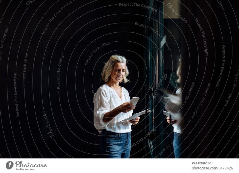 Lässig reife Geschäftsfrau mit Smartphone am Fenster im Loft-Büro Job Berufe Berufstätigkeit Beschäftigung Jobs geschäftlich Geschäftsleben Geschäftswelt
