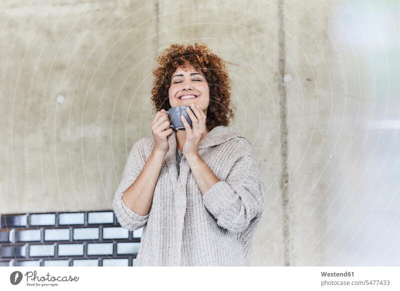 Lächelnde Frau, die einen Kaffee an einer Betonwand genießt Betonwände Betonwaende weiblich Frauen genießen geniessen Genuss Portrait Porträts Portraits lächeln