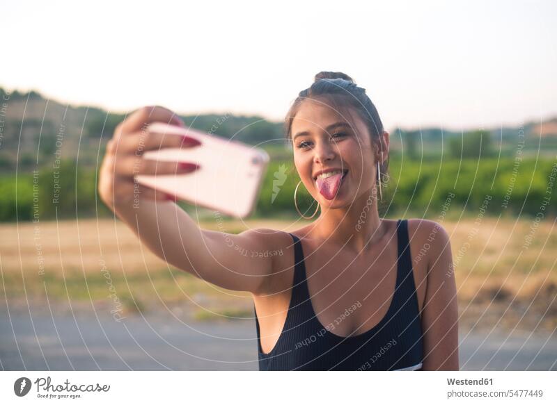 Porträt eines Teenagers, der ein Selfie mit seinem Smartphone macht und dabei die Zunge herausstreckt Selfies Teenagerin junges Mädchen Teenagerinnen weiblich