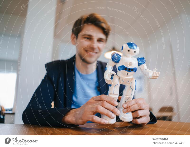 Lächelnder Mann hält Roboter Männer männlich Tisch Tische halten lächeln Erwachsener erwachsen Mensch Menschen Leute People Personen Maschine Automat