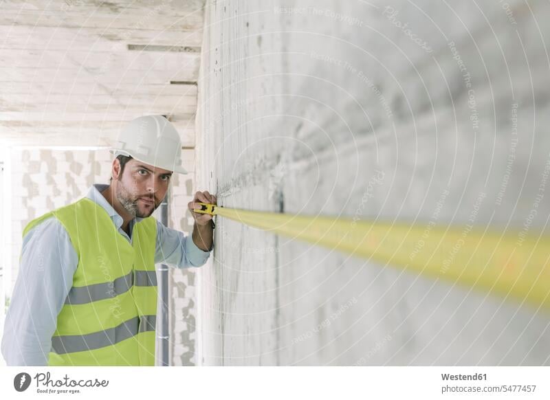 Architekt beim Messen einer Wand auf der Baustelle Job Berufe Berufstätigkeit Beschäftigung Jobs Architekten Berufsbekleidung Massband Messband Metermaß Arbeit