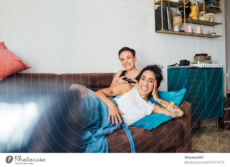 Lächelndes lesbisches Paar beim Fernsehen auf dem Sofa Farbaufnahme Farbe Farbfoto Farbphoto Innenaufnahme Innenaufnahmen innen drinnen Tag Tageslichtaufnahme