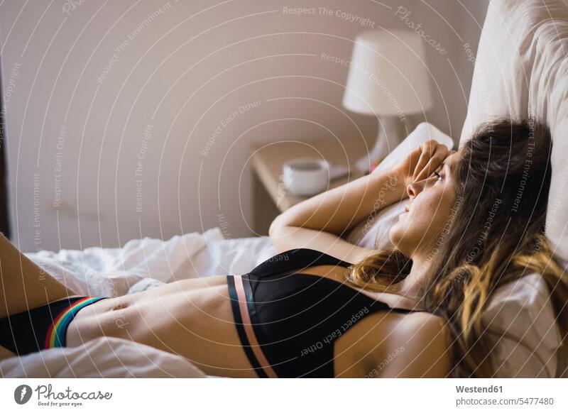 Tagträumende junge Frau in Unterwäsche auf dem Bett liegend Betten liegt Verträumt träumerisch weiblich Frauen tagträumen Tagtraum Erwachsener erwachsen Mensch
