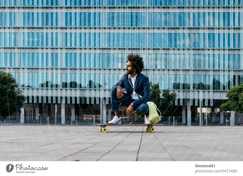 Spanien, Barcelona, junger Geschäftsmann hockend auf Skateboard in der Stadt Businessmann Businessmänner Geschäftsmänner kauernd Mann Männer männlich
