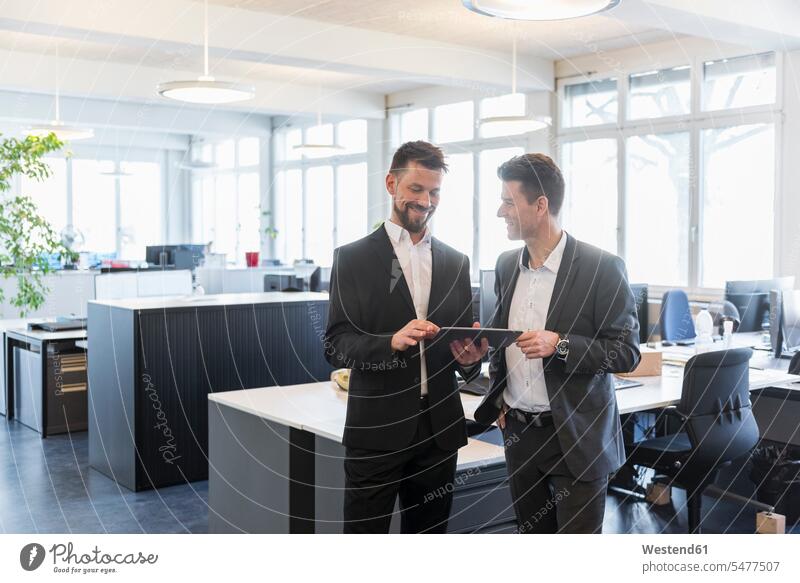 Zwei Geschäftsleute stehen im Büro, diskutieren Lösungen und benutzen ein digitales Tablett Tablet Computer Tablet-PC Tablet PC iPad Tablet-Computer