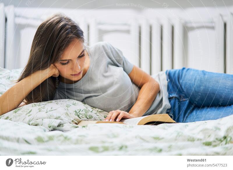 Junge Frau zu Hause liegt im Bett und liest Buch Zuhause lesen liegen Erwachsener Mensch Hygge Kopf aufstützen genießen Entschleunigung Hobby Gemütlich Freizeit