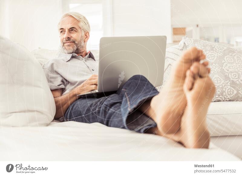 Reifer Mann benutzt Laptop zu Hause auf der Couch geschäftlich Geschäftsleben Geschäftswelt Geschäftsperson Geschäftspersonen Businessmann Businessmänner