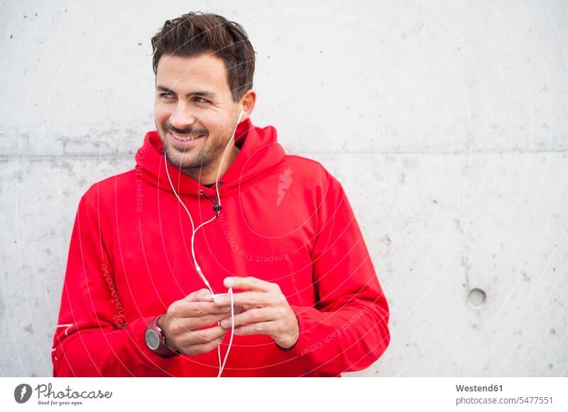 Porträt eines sportlichen jungen Mannes, der an einer Betonwand Musik hört entspannen relaxen hoeren freuen Farben Farbtoene Farbton Farbtöne rote roter rotes