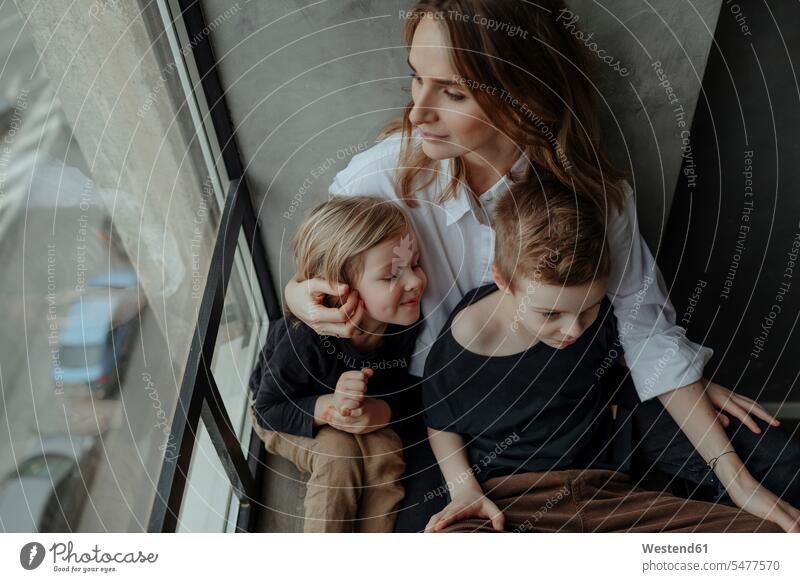 Schrägansicht einer Frau, die mit ihren Söhnen zu Hause am Fenster sitzt Farbaufnahme Farbe Farbfoto Farbphoto Innenaufnahme Innenaufnahmen innen drinnen