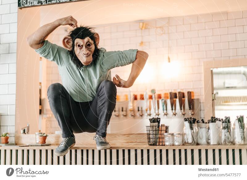 Mann mit Affenmaske, sitzt auf dem Tresen einer Bar und kratzt sich am Kopf sitzen sitzend Bars Unternehmer Arbeitgeber Start-up Startups Start ups Start-ups