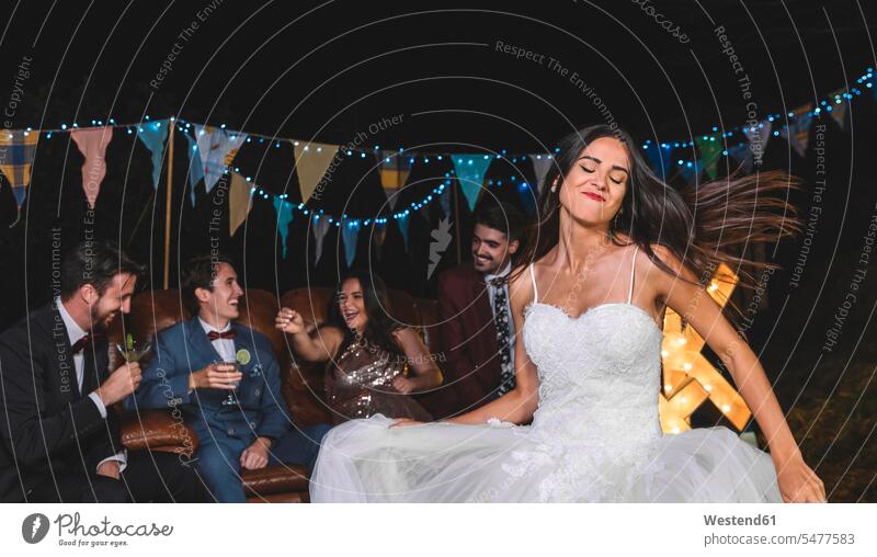 Glückliche Braut tanzt auf einer nächtlichen Feldfeier mit Bräutigam und Freunden im Hintergrund tanzen tanzend Bräute Hochzeit heiraten Heirat Hochzeiten Party